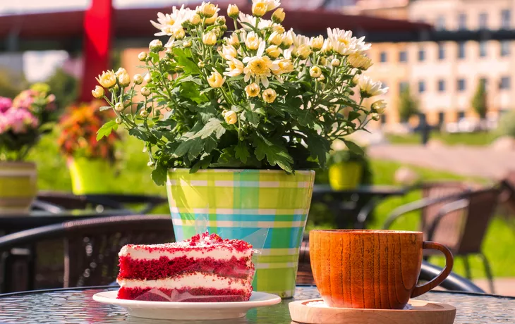 Tisch in einem Straßencafé mit Kaffee und Kuchen und einem Strauß gelber Chrysanthemen